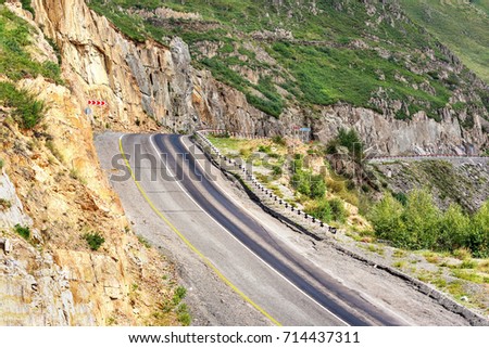 Colorful view on the steep turn of the asphalt road in the mountains running along the rocks, green grass and trees on the slopes
