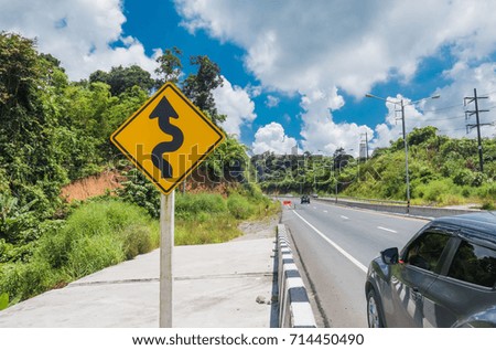 Yellow sign with winding road symbol in the countryside and sky background .