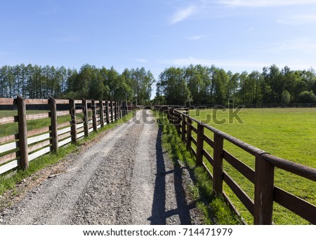 a rural sandy road fenced with an old village fence. photo of summer on a background of blue sky