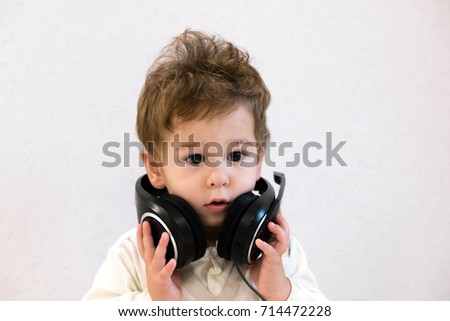 Pop music. Happy smiling baby listens to music in headphones on gray background. Cheerful portrait. Little Adorable baby boy with big headphones. funny serious emotions. listen carefully information