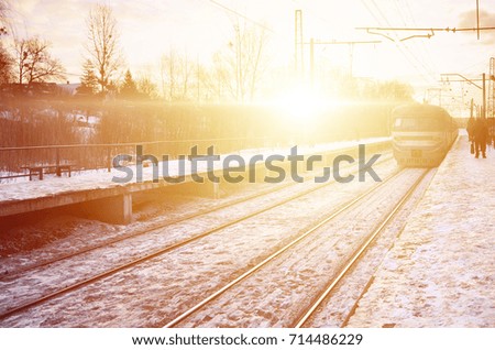 Photo of bright and beautiful sunset on a cloudy sky in cold winter season. Railway track with platforms for waiting trains and power transmission lines in the middle of winter forest landscape