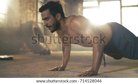 Muscular Shirtless Man Covered in Sweat Does Push-ups in a Deserted Factory Remodeled into Gym. Part of His Fitness Workout/ High-Intensity Interval Training. Royalty-Free Stock Photo #714528046