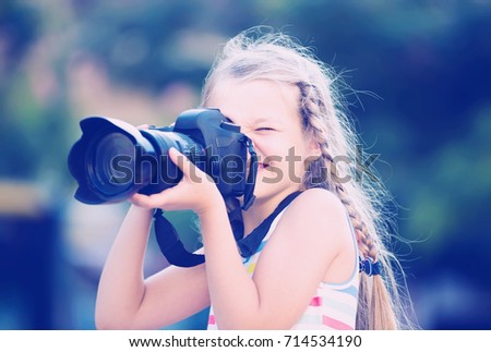 happy female child taking pictures with camera in park on summer day