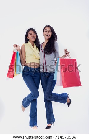 Pictures of two beautiful cheerful girls in summer dress, holding dollar bills with shopping bags and looking at camera through white background.