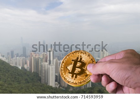 Hand holding a bitcoin with the Skyline of Hong Kong in the background. Hong Kong is considered the financial and business capital of Asia
