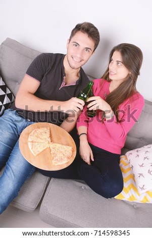 Beautiful young couple drinking beer and eating pizza. Indoors.