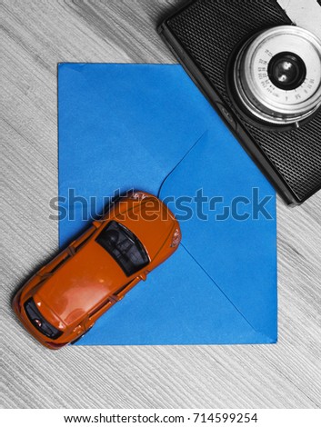 Black and white photo with orange toy car and blue envelope on wooden background