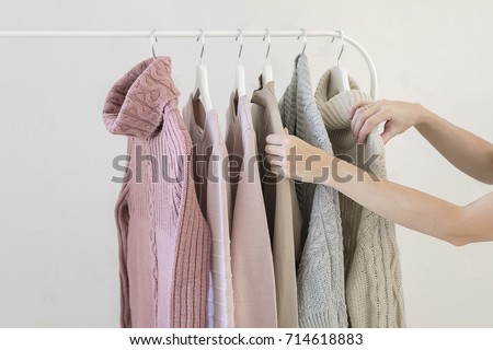 Woman choosing pastel warm cozy sweaters on hangers