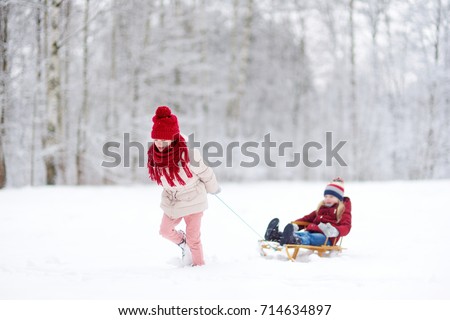 Two funny little girls having fun with a sleight in beautiful winter park. Cute children playing in a snow. Winter activities for kids.