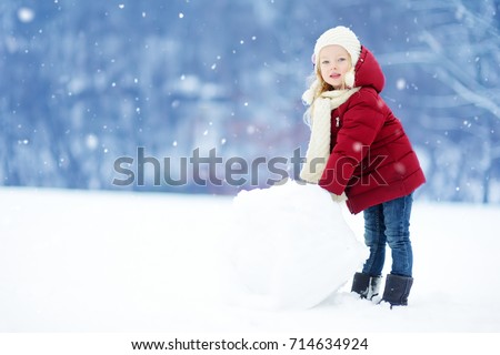 Adorable little girl building a snowman in beautiful winter park. Cute child playing in a snow. Winter activities for kids.