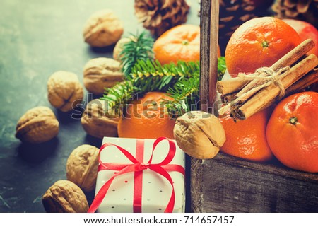 Christmas Gift Box with Red Silk Ribbon Tangerines Cinnamon Sticks Fir Tree Branches Pine Cones Walnuts in Wood Box Black Background Greeting Card Poster Copy Space