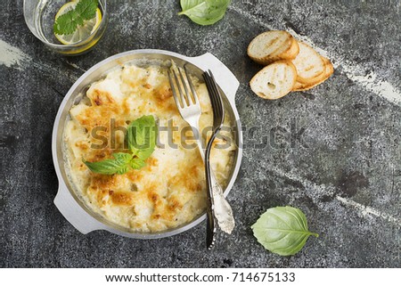 Fragrant homemade casserole with cod and onion in cream sauce with horseradish under a cheese ruddy crust in a form on a gray background with crispy grilled toast. Top View