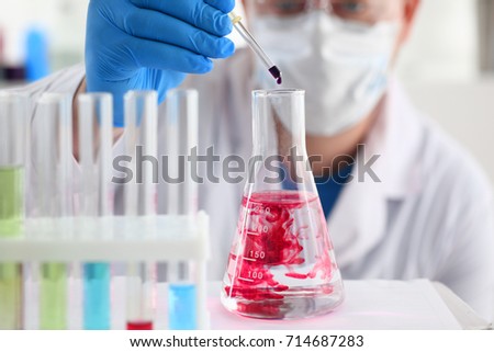 A male chemist holds test tube of glass in his hand overflows a liquid solution of potassium permanganate conducts an analysis of water samples versions of reagents using chemical manufacturing Royalty-Free Stock Photo #714687283