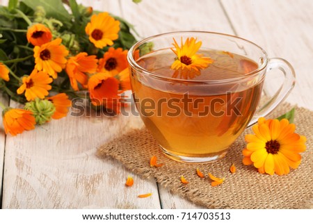 Calendula tea with fresh flowers on white wooden background