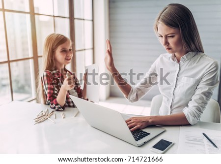I'm busy! Beautiful young woman is working at home with her little cute daughter nearby. Don't have enough time for child. Royalty-Free Stock Photo #714721666