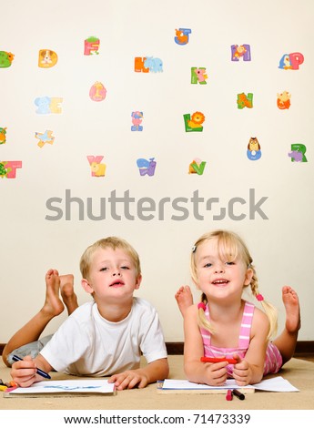 cute kids lying on the floor of a playschool with crayons and smiling at the camera