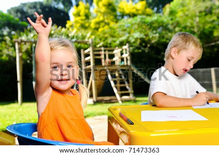 cute blonde girl holds hand up for attention at kindergarten