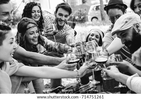 Group of people cheering with red glasses of wine - Happy young friends enjoying picnic in a park with food e drink - Black and white edit - Youth concept - Focus on woman with band on the left