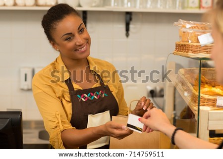 Attractive female baker taking a credit card from her customer profession occupation service salesperson selling consumerism client service friendly bill check manager small business owner banking