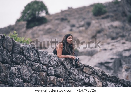A woman stands in a mountain area and poses with vintage photo camera...