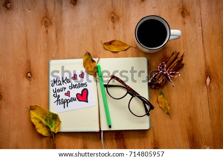 Cup of coffee and an open notebook with blank pages ,pair of glasses and make your dreams happen on a note on rustic wooden table with Autumn leaves