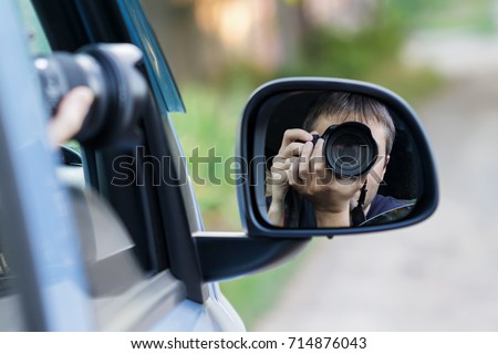 A man is taking photo someone or something from an open car window. Reflection in the side mirror of the car