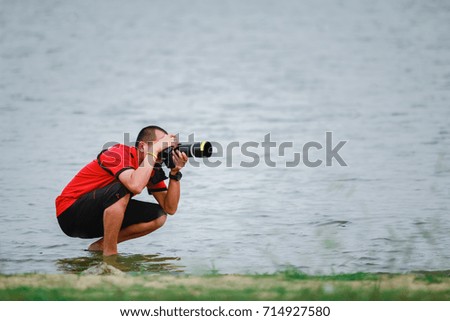 A man is using a camera, taking a picture of nature in a reservoir.
Male photographers wearing red robes are recording wildlife.
