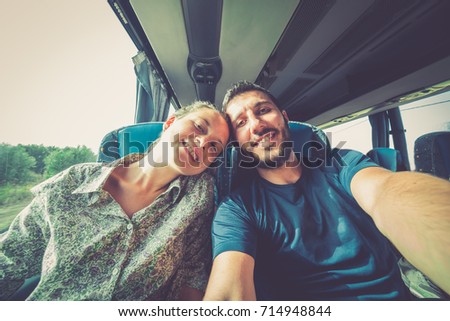 Backpackers traveling around the world on the bus. Young handsome man with his girlfriend on traditional bus taking selfie on smartphone.
