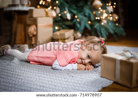 In Christmas curly little girl lying near the fireplace with gifts.