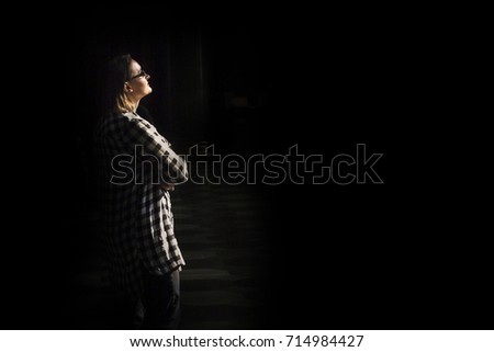 Woman's silhouette under light on black background with copy space right. Female specialist praying in church