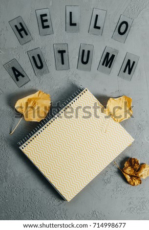 Cozy composition: yellow notebook, leaves, letters Hello autumn on gray background. Top view, flat lay