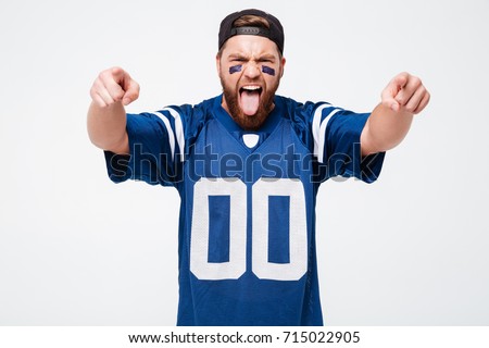 Picture of emotional man fan in blue t-shirt standing isolated over white background. Looking camera showing tongue pointing at you.