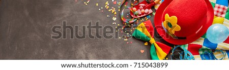 Bright red carnival hat and bow tie panorama with balloons, confetti and copy space on slate for a wide banner or header
