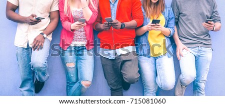 Teenagers texting mobile phone messages leaning on urban wall - Group of multiracial friends using cellular standing outdoors - Concept of students addiction to social network and telephone technology Royalty-Free Stock Photo #715081060