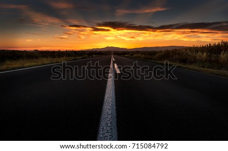 Straight highway road to a dramatic fiery sunset Royalty-Free Stock Photo #715084792