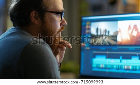 Male Video Editor Works with Footage and Sound on His Personal Computer. He Works in a Cool Office Loft. Royalty-Free Stock Photo #715099993