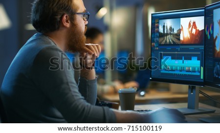 Male Video Editor Works with Footage and Sound on His Personal Computer with Two Displays. He Works in a Cool Office Loft with Other Creative People.
