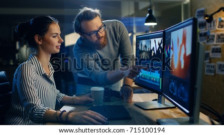 Female Video and Sound Editor Works With Her Male Colleague on a Project on Her Personal Computer with Two Displays. They Work in a Creative Loft Office. Royalty-Free Stock Photo #715100194