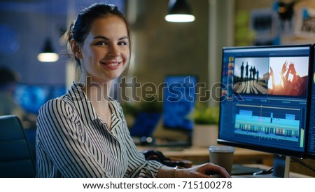 Female Video Editor Turns and Warmly Smiles into the Camera. Her Office is Modern and Creative Loft Studio.