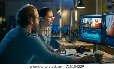 Beautiful Female and Handsome Male Video Editors Discuss Footage They're Working On. They Enjoy Working Together in a Cozy Creative Studio. Royalty-Free Stock Photo #715104229