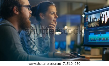 Female and Male Video Editors Work With Footage and Sound on Their Personal Computer with Two Displays. They are Beautiful and Creative People and Their Office is Modern Loft. Royalty-Free Stock Photo #715104250
