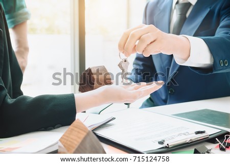 real estate agent holding house key to his client after signing contract agreement in office,concept for real estate, moving home or renting property
