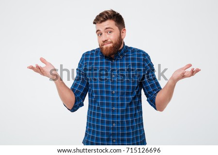 Confused young bearded man standing and shrugging shoulders isolated over white background Royalty-Free Stock Photo #715126696