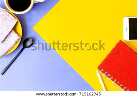 Pastel office desk with smart phone, red notebook, bread, spoon and a cup of black coffee on two tone background