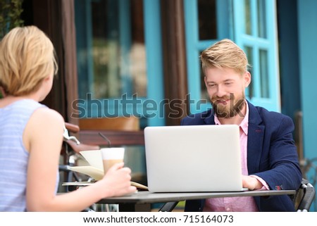 Young blogger with with woman sitting in cafe, outdoors