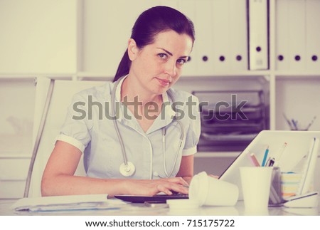 Young and smiling doctor in uniform near laptop with stethoscope