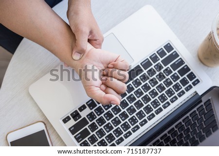 Close up woman holding and pressing or touching her wrist while working with laptop in the office. Numbness or pain on wrist concept.
