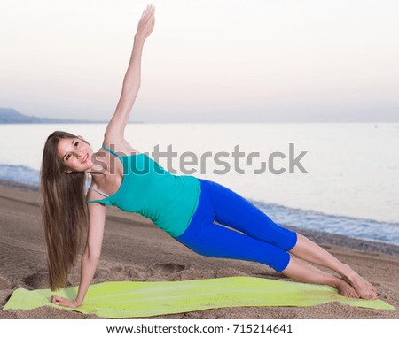 Female 20-25 years old is doing excercises on endurance on the beach near sea.