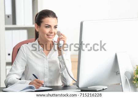 Young female receptionist talking on phone in office Royalty-Free Stock Photo #715216228