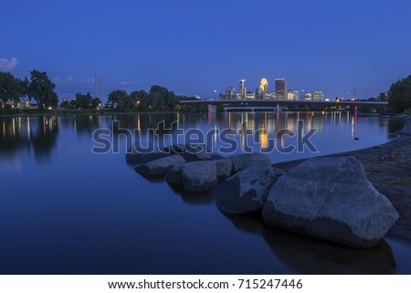 A Wide Angle Twilight Long Exposure of the Calm Mississippi River Reflecting Shoreline Rocks and Distant Cityscape